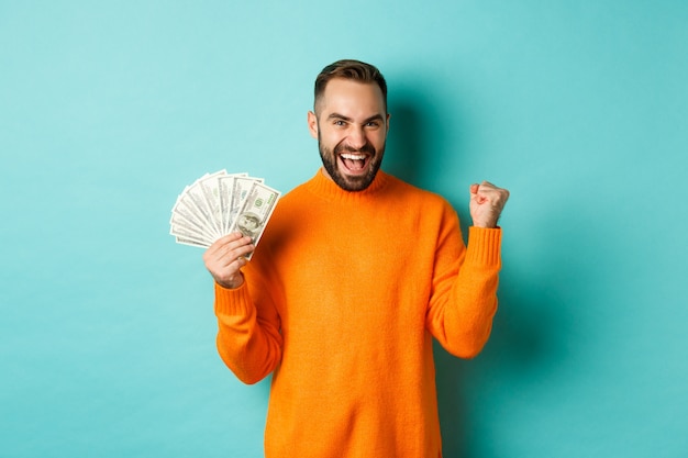 Free photo shopping. cheerful guy holding money, winning prize in cash and making fist pump, triumphing