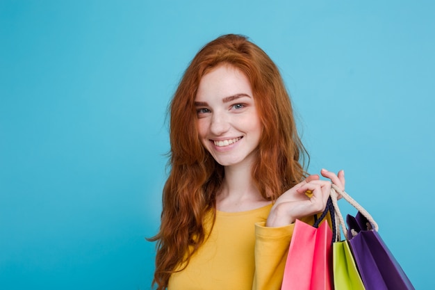 Free Photo shopping concept - close up portrait young beautiful attractive redhair girl smiling looking at camera with shopping bag. blue pastel background. copy space.