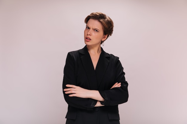 Free Photo short haired woman in suit looks into camera with misunderstanding. lady in black jacket poses in bad mood on isolated background