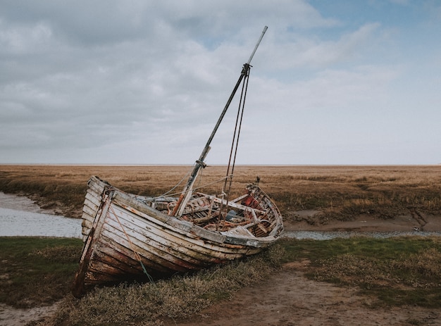 Free Photo shot of an abandoned broken boat left by the riverbank surrounded by a wheat field