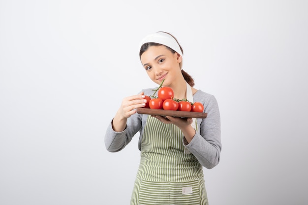 Shot of adorable young woman holding plate of red tomatoes over white wall