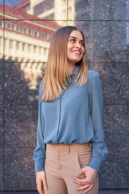 Shot of beautiful young businesswoman wearing blue chiffon shirt while standing and posing on gray marble wall