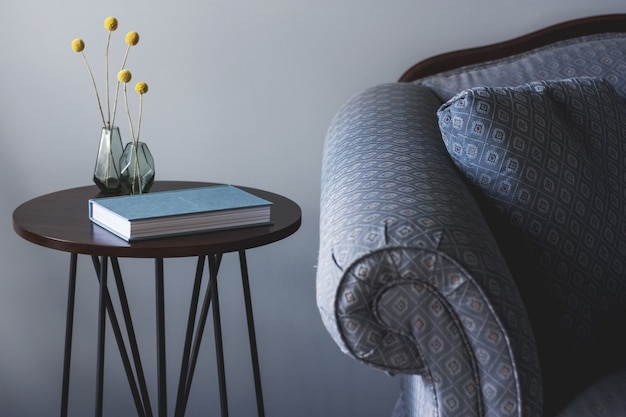 Free Photo shot of a blue sofa near a small round table with a book and two vases with yellow plants on it