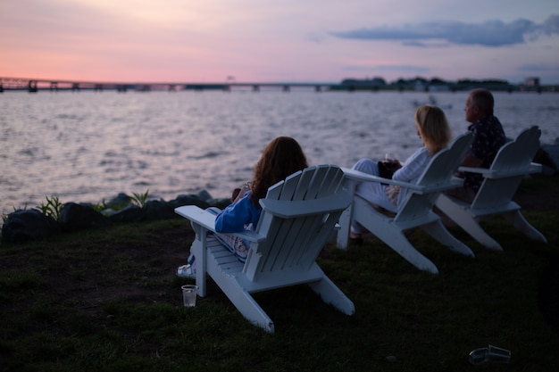 Free photo shot of people sitting on white chairs across body of water