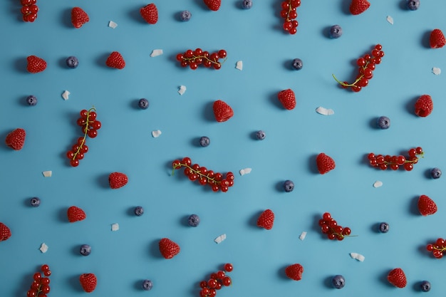 Free Photo above shot of tasty appetizing ripe berries for eating or making desserts. fresh raspberry redcurrant, blueberry and coconut pieces on blue background. mix fruits for your healthy nutrition.