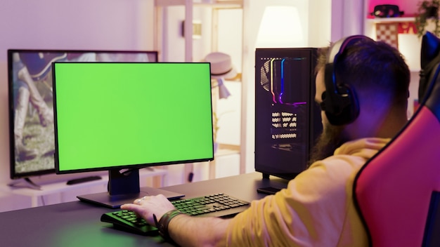 Over shoulder footage of man playing video games on computer with green screen. Professional game player.