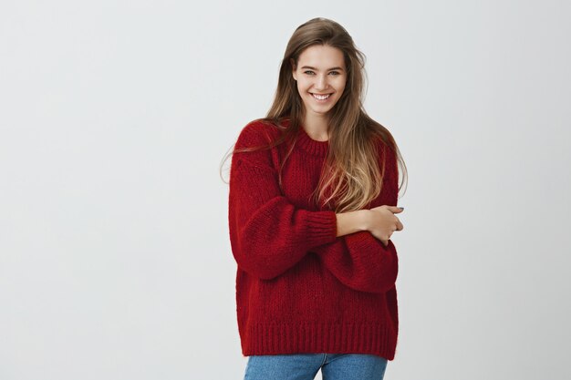 Show me what you have got. Studio shot of positive beautiful caucasian girl in trendy outfit standing with crossed hands and smiling from positive emotions 