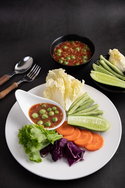 Shrimp-paste sauce in a bowl on the white plate with cucumber, yard long bean, thai eggplant, fried white cabbage, carrots and salad