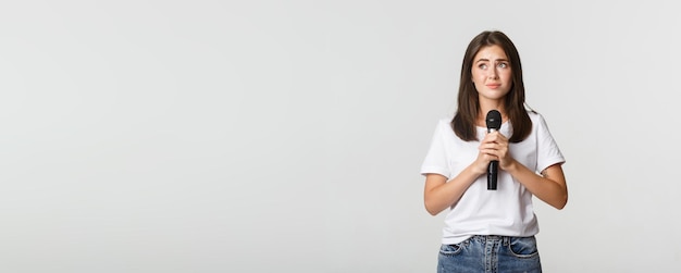 Free photo shy cute brunette girl scared of singing in public standing with microphone and looking nervous