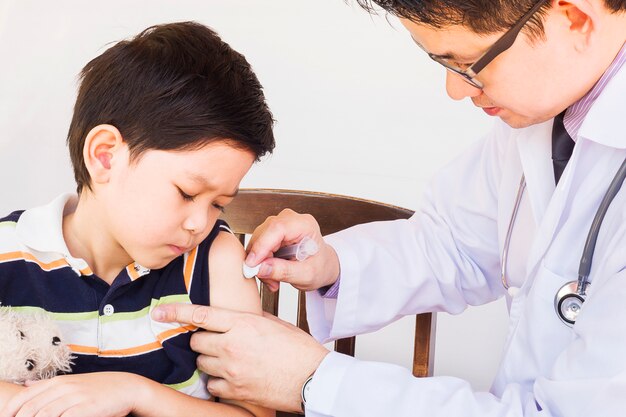 Sick Asian boy being treated by male doctor over white background