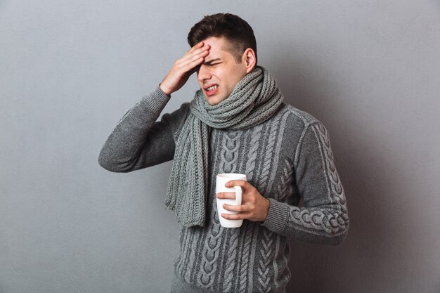 Sick Man in sweater and scarf having headache while holding cup of tea