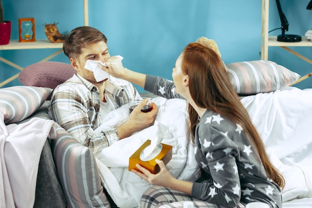 Sick man with fever lying in bed having temperature. The his wife take care for him. 