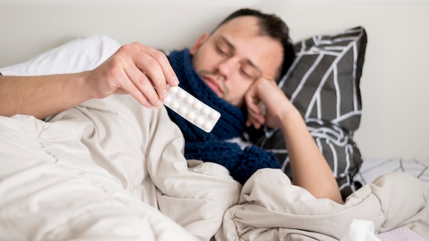 Free photo sick person staying in bed and looking at pills