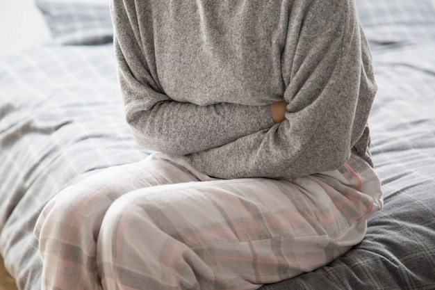 Sick woman on bed keeping hands on stomach, suffering from pain