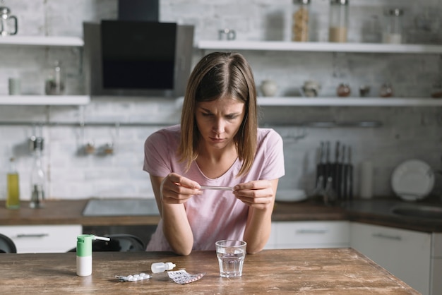 Free Photo sick woman checking temperature on thermometer with medicines on wooden desk