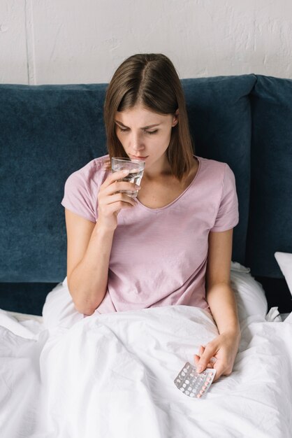 Sick woman drinking water while taking pills