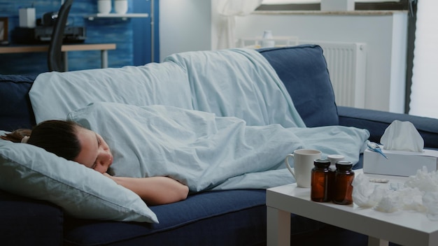 Free Photo sick woman laying on couch with blanket feeling cold and having virus symptoms. adult with seasonal flu sleeping, having medication on table. tired ill person with chills and shivering