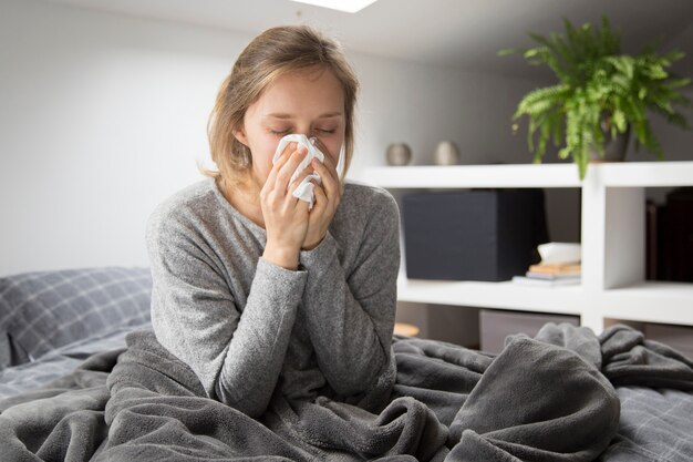 Sick woman sitting in bed, blowing nose with napkin