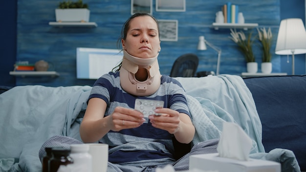 Sick woman with cervical neck foam reading label of medication pills