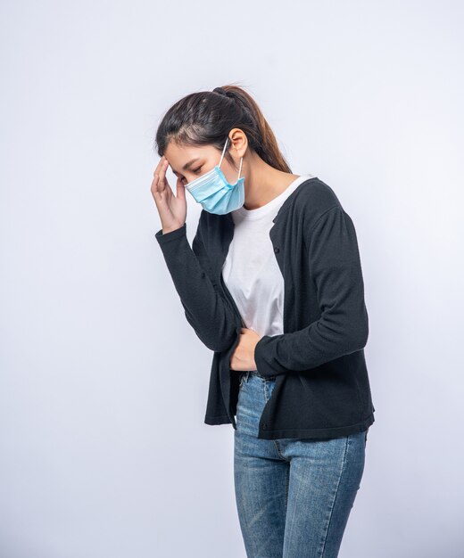 A sick woman with a headache wore a mask and placed a hand on her head.