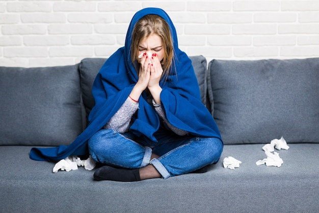 Free photo sick woman with rheum and headache holding napkin, sitting on sofa with coverlet and pills at home