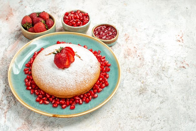 Side close-up view appetizing cake cake of strawberries and pomegranate and the bowls of berries on the table