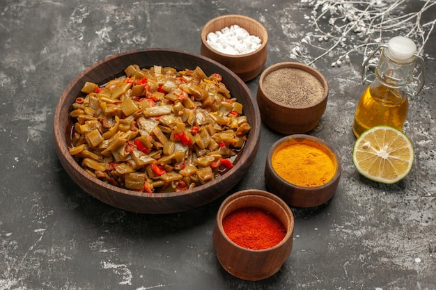 Free Photo side close-up view appetizing dish plate of the appetizing green beans and tomatoes next to four bowls of spices bottle of oil and half a lime on the dark table