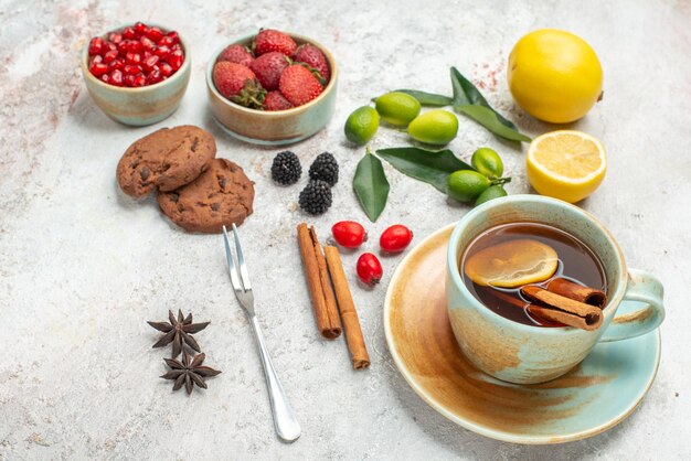 Side close-up view berries cookies star anise cookies strawberries white cup of tea citrus fruits cinnamon sticks fork on the table