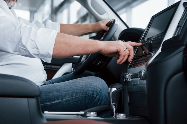 Side close up view. Businessman in official clothes sits in a luxury car and pushing the buttons on the music player