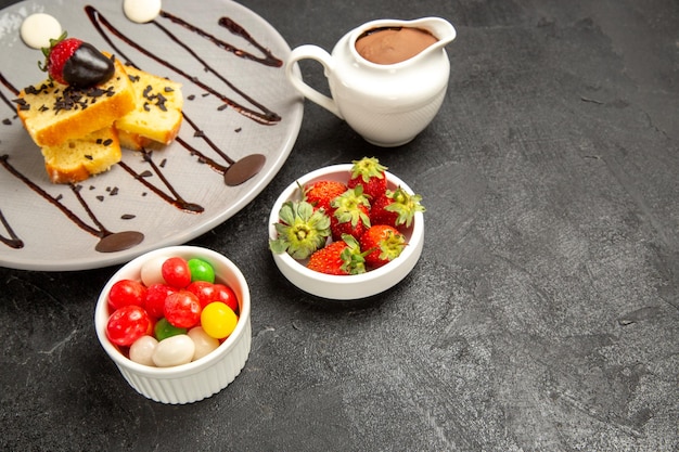 Side close-up view cake with chocolate cake with chocolate and strawberries next to the bowls of strawberries and sweets