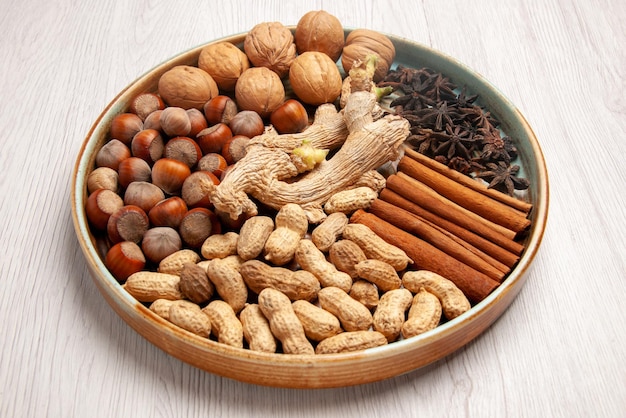 Side close-up view cinnamon sticks cinnamon sticks hazelnuts walnuts peanuts and star anise on the white table