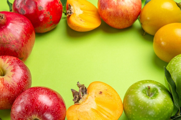 Free Photo side close-up view colorful fruits pomegranate apples persimmons and leaves on the table