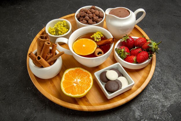 Side close-up view a cup of tea with sweets chocolate cream a cup of tea lemon strawberries chocolate and hizelnuts in the wooden plate