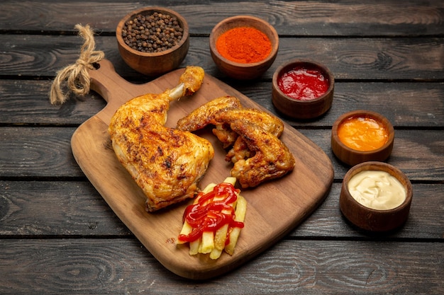 Side close-up view french fries chicken french fries and bowls of colorful sauces and spices on the dark table