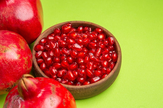 Side close-up view fruits brown bowl of the appetizing seeds of pomegranate on the green table