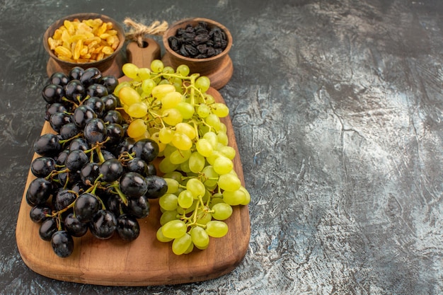 Free photo side close-up view fruits bunches of green and black grapes on the board bowls of dried fruits