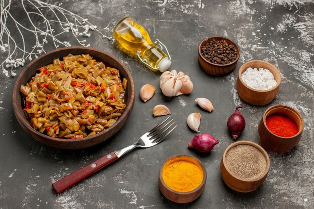 Free photo side close-up view green beans and spices green beans in the bowl next to the fork garlic onion bowls of colorful spices and bottle of oil on the table