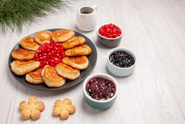 Side close-up view pancakes pancakes and pomegranate in the plate next to the bowls of berries cookies sauce and Christmas tree on the table