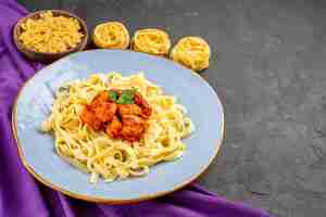 Free photo side close-up view pasta with gravy appetizing pasta with gravy and meat on the plate next to the different kinds of pasta on the purple tablecloth