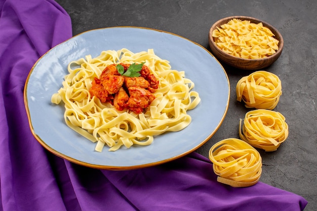 Free photo side close-up view pasta with gravy plate of an appetizing pasta with gravy and meat next to the bowls of pasta on the purple tablecloth