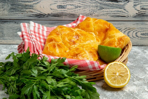 Side close-up view pies and lemons wooden basket of appetizing pies herbs lemon and lime and tablecloth on the wooden background