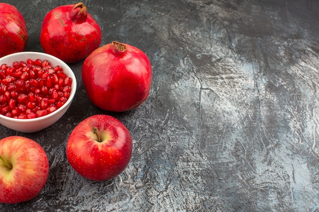 Free photo side close-up view pomegranates apples pomegranates around a bowl of seeds of pomegranate