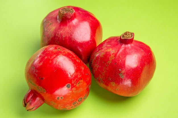 Side close-up view pomegranates three pomegranates on the green surface