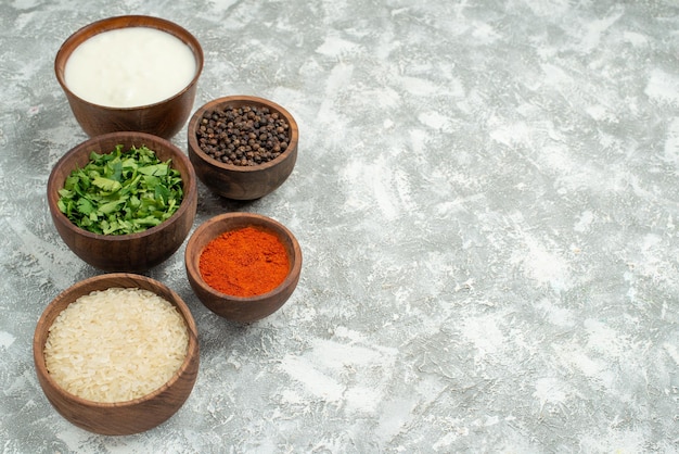 Free Photo side close-up view spices rice herbs rice spices herbs black pepper and sour cream in bowls on the left side of the table