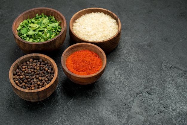 Side close-up view spices on table herbs spices rice and black pepper in bowls on the left side of the black table