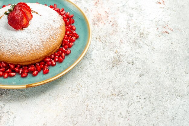 Side close-up view strawberry pomegranate blue plate of the appetizing cake with strawberries and pomegranate on the grey table