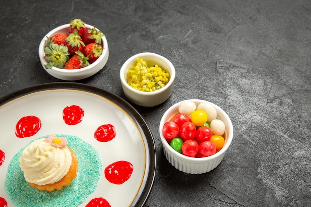 Side close-up view sweets in bowls bowls of sweets and appetizing strawberries next to the plate of cake with colorful sauces on the black table