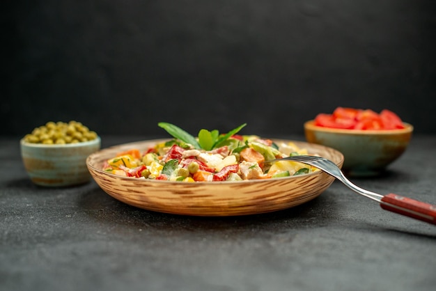 Free photo side close view of bowl of vegetable salad with fork and bowls of vegetables on side on dark grey table on dark grey background