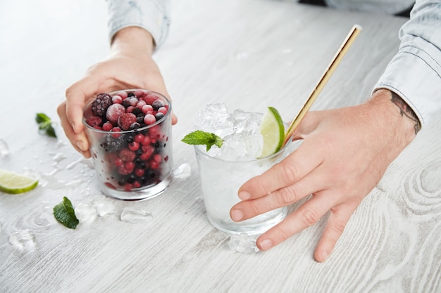 Free Photo side close view man hands hold glasses with frozen berries and ice cubes with lime