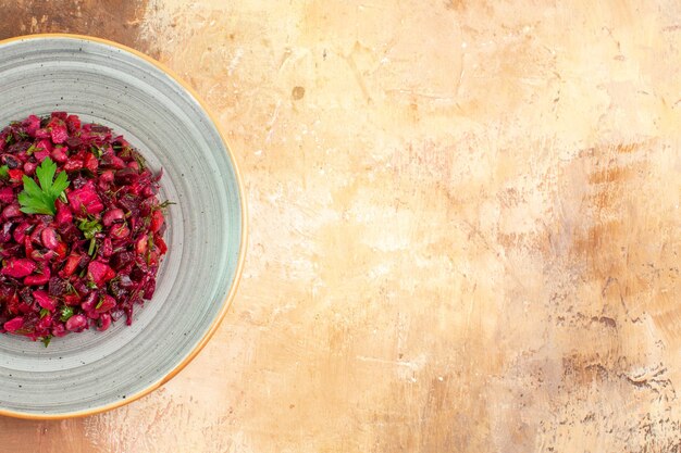 Side close view of plate of a red salad with greens on it on a wooden backgorund